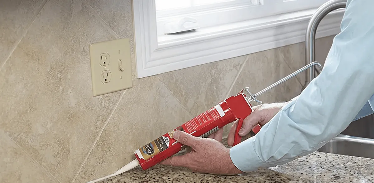 Handyman applying caulk along a kitchen backsplash and countertop seam in Detroit, MI