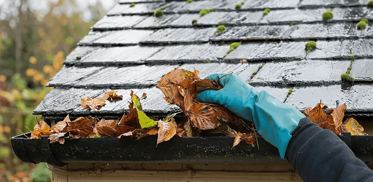 Gutter cleaning technician clearing wet leaves from roof gutters in Detroit, MI